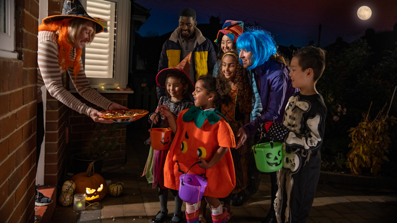 Children and chaperone at door trick or treating dressed in costumes.