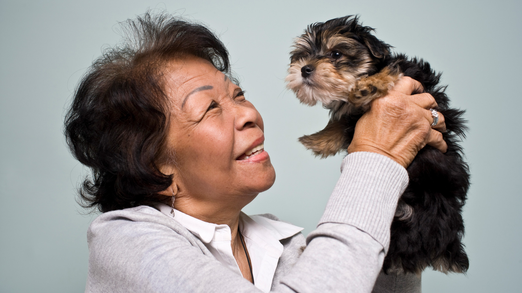 Senior woman holding small puppy while smiling.