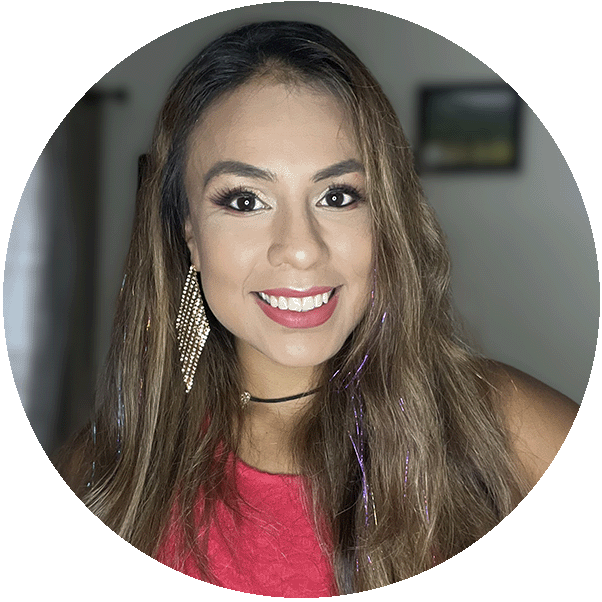 Photograph of a person with long, light brown hair wearing a sleeveless red top and a black choker necklace. The background shows a room with a window covered by curtains and a framed picture on the wall.